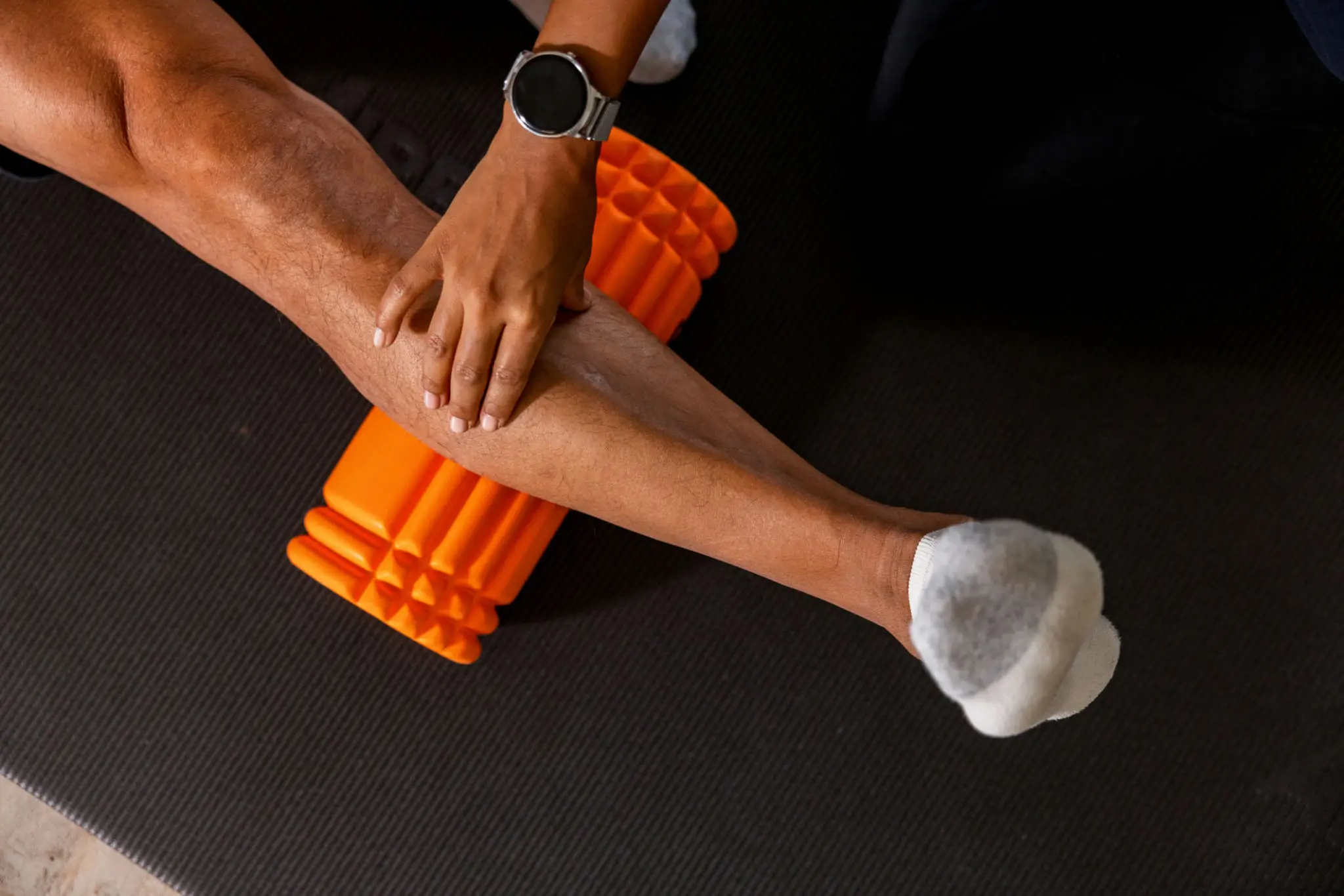 Person using an orange foam roller on their calf muscle.