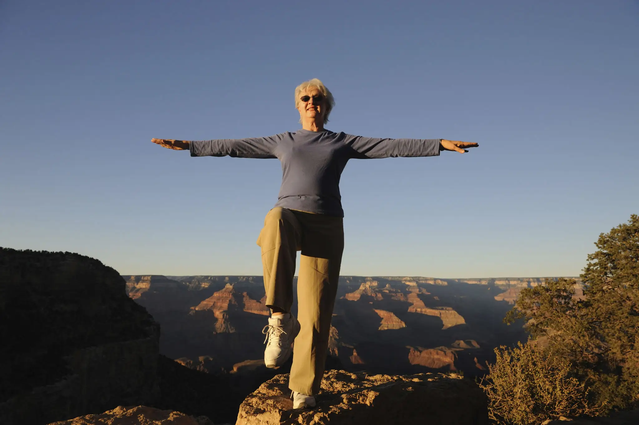 Person standing with arms outstretched at a scenic canyon viewpoint.