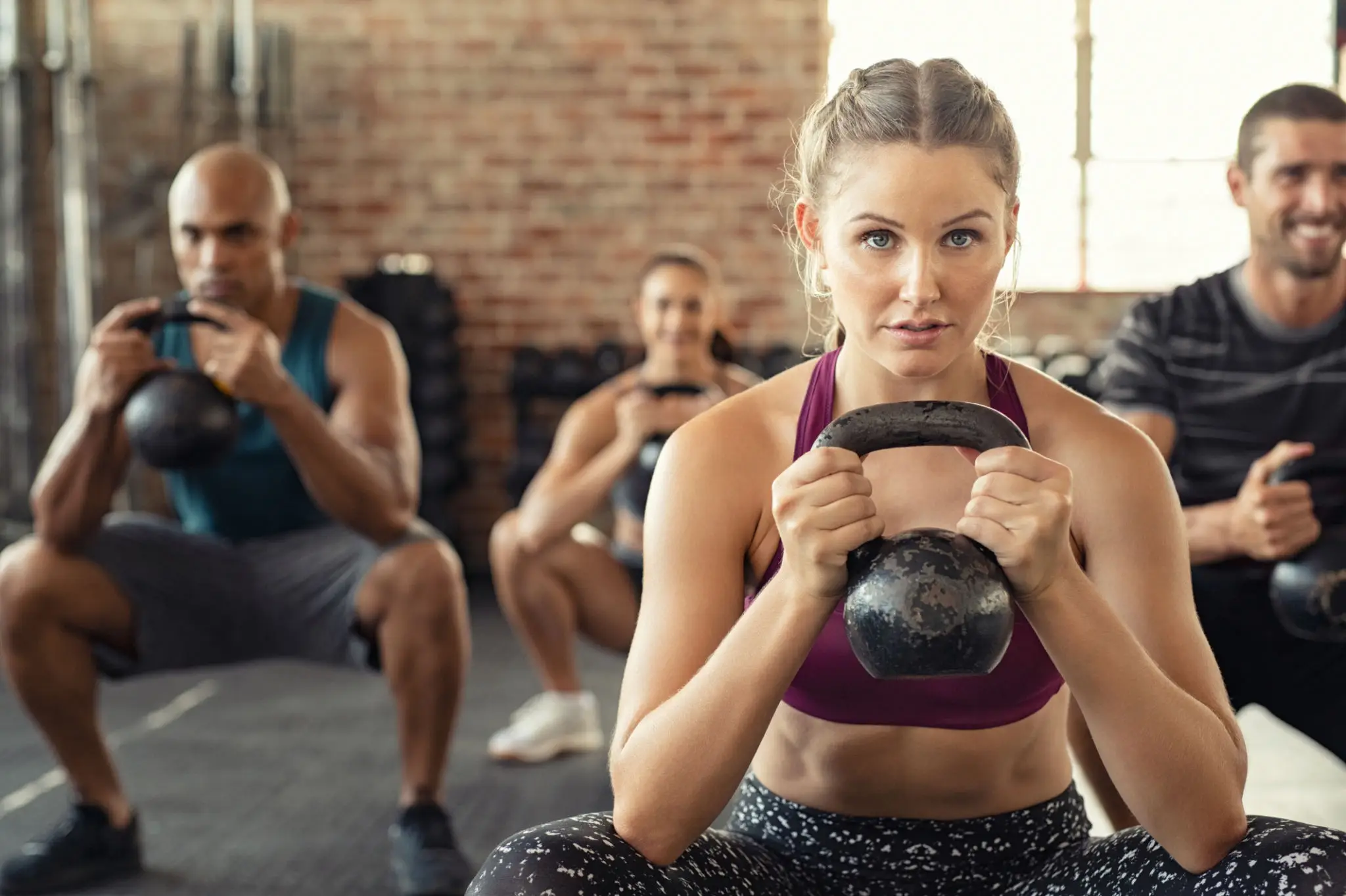 A focused woman lifting a kettlebell in a gym class.