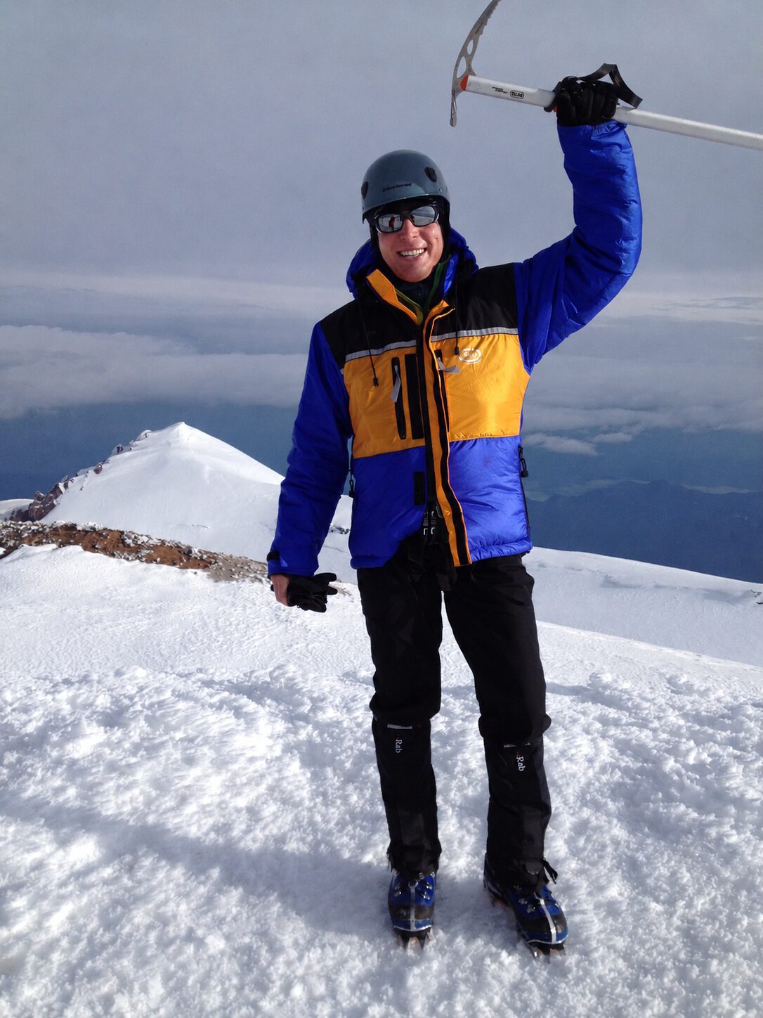Person in winter gear waving on a snowy mountain peak.